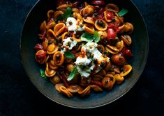 a bowl filled with pasta and vegetables on top of a black table next to a fork