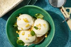 three scoops of ice cream in a green bowl on a blue tablecloth next to a spoon