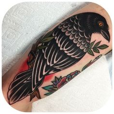 a black bird sitting on top of a person's leg with leaves around it