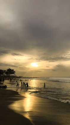 people walking on the beach at sunset with dark clouds in the sky and sun reflecting off the water