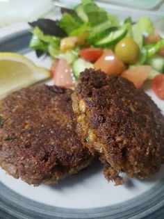 two patties on a plate with salad and lemon wedges