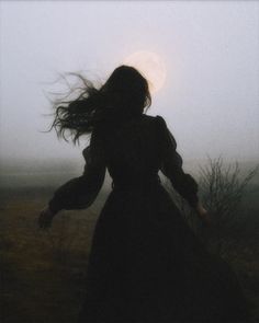 a woman with long hair is walking in the fog