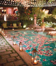 candles are lit in front of an outdoor pool with flowers and lights on the water