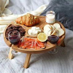 a wooden tray with bread, cheese and fruit on it sitting on top of a bed next to a glass of wine