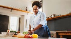 a woman in the kitchen chopping vegetables on a cutting board