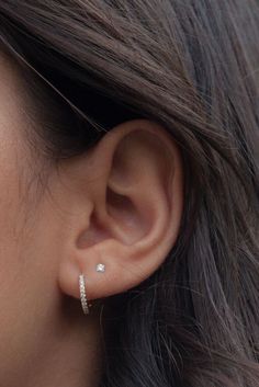 a close up view of a woman's ear with two small diamond hoops