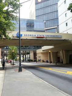 people are walking on the sidewalk under an overpass in front of a college building