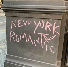 a chalkboard with the words new york romantic written on it in pink ink next to a street corner