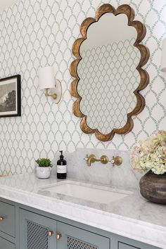 a bathroom vanity with a large mirror above it and a vase full of flowers on the counter