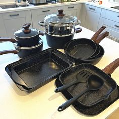 black pots and pans are sitting on the kitchen counter with wooden utensils