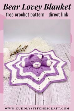 a purple and white crocheted blanket with balls on it, next to a teddy bear