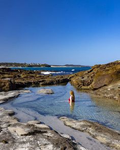 a person wading in the water near some rocks