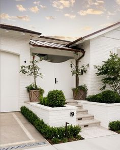 a white house with some plants in the front yard and stairs leading up to it