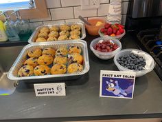 fruit and muffins are sitting on the counter in front of other dishes with signs