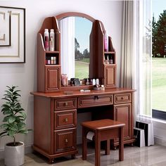 a wooden desk with a mirror and stool in front of a window next to a potted plant