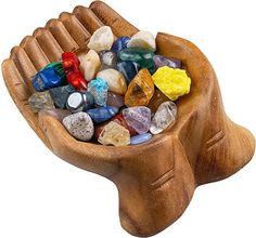 a wooden bowl filled with lots of colorful rocks and stones on top of a white background