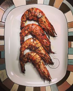 three cooked shrimp on a white plate with colorful mosaic tiles in the backround