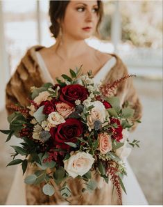 a woman in a wedding dress holding a bouquet with red and white flowers on it