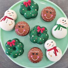 a green plate topped with donuts covered in frosting and decorated like snowmen