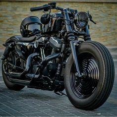 a black motorcycle parked on top of a brick road next to a building with a helmet on it's back end