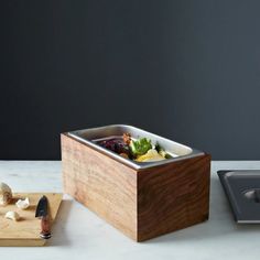 a wooden cutting board topped with food next to a container filled with fruit and vegetables