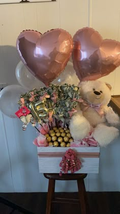 a teddy bear sitting on top of a box filled with chocolates and balloons in the shape of hearts