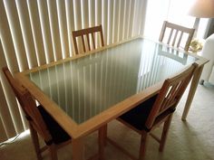 a glass table with wooden chairs in front of a sliding door and blinds on the window