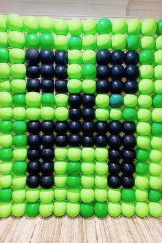 a large green and black letter made out of balloons on top of a wooden floor