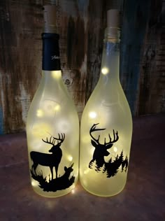 two lighted wine bottles with deer and trees on them