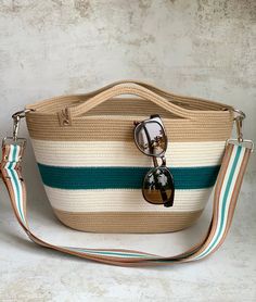 a white and green striped bag with sunglasses on it's handle, sitting against a wall