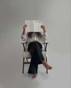 a woman sitting in a chair holding up a book over her head with both hands