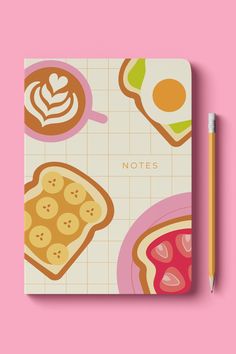 a notebook with food illustrations on it and a pencil next to it, against a pink background