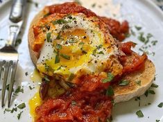 an egg is on top of bread with tomato sauce and parsley sprinkled around it