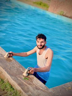 a man standing on the edge of a swimming pool holding onto a rope that is attached to a wall