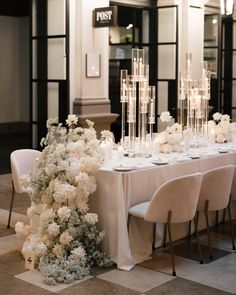 the table is set up with white flowers and candles for an elegant dinner party or reception