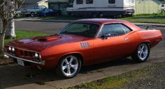 an orange muscle car is parked on the side of the road in front of some grass