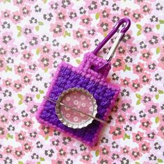 a pink and purple crocheted square with a button on it sitting on top of a flowered surface