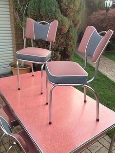 three pink and gray chairs sitting on top of a metal table in front of a house