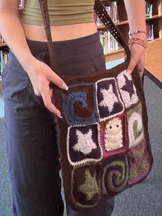 a woman holding a crocheted purse in front of a bookshelf