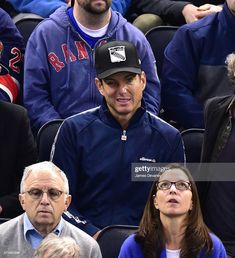 two men and a woman sitting in the stands at a baseball game, one wearing a hat