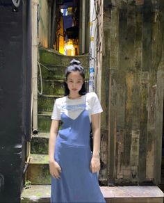 a woman standing in front of an old set of stairs wearing a blue dress and white t - shirt