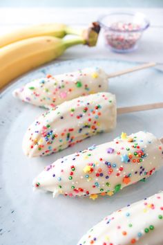 some cake pops with sprinkles are on a blue plate next to bananas