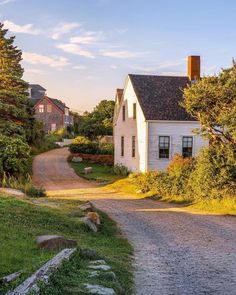 an old white house sitting on the side of a road next to trees and grass