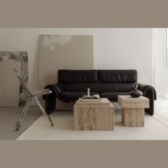 a black leather couch and two stools in a living room with a large painting on the wall