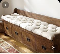 an old wooden bench with white cushions and drawers on it's sides, in front of a wall