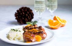 a white plate topped with meat covered in sauce next to mashed potatoes and orange slices