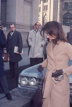 a woman standing in front of a car with other people around her looking at it