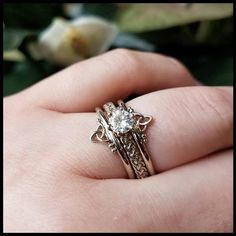 a woman's hand holding a gold ring with a diamond in the center and filigrees around it