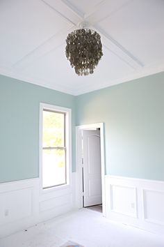 an empty room with a chandelier hanging from the ceiling and white trim on the walls