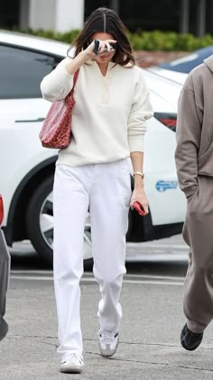 a woman walking down the street while holding a red handbag and looking through binoculars